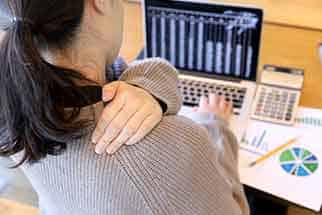 Person holding a painful shoulder at a desk